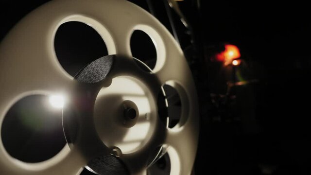 Close-up of a reel with a film rotating and light rays. Old 8mm film projector working in the night in a room