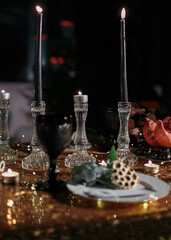 Medium sharp.Front view of a decorated with a golden tablecloth on a table with burning black candles with pomegranate, grapes, binoculars and ceremonial table setting at wedding reception in twilight