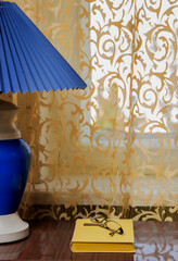 The lamp with shade, a book and a window with a curtain.
