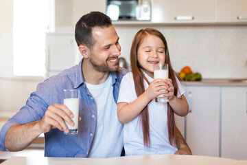 Father And Daughter Drinking Milk Sitting At Table In Kitchen