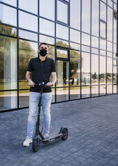Fototapeta na wymiar Vertical full length portrait of student on electric scooter, kick scooter or e-scooter. Man wear mask to protect himself from second wave of epidemic corona virus. Urban transportation concept.