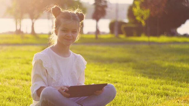 Little girl playing Minecraft on tablet in a park on a sunny summer day