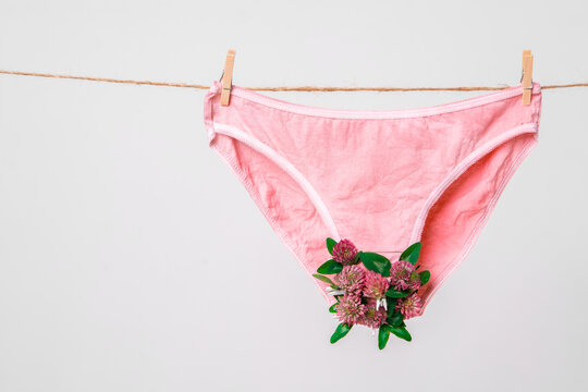 Pink women's underwear decorated with flowers on clothesline isolated on white, concept photography for feminist blog