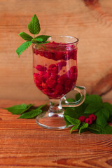 Summer raspberry cold tea in a glass on wooden background. Healthy fruit cocktail. Tasty red juice with fresh green leaves. Seasonal raspberries vitamins, colds and flu treatment hot drink. Food photo