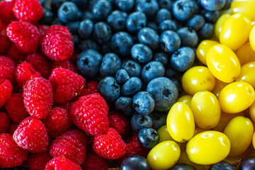 View from above. A mix of yellow, red and blue berries in a white grater. Triangle separation. Summer mix of fruits. Berry layout