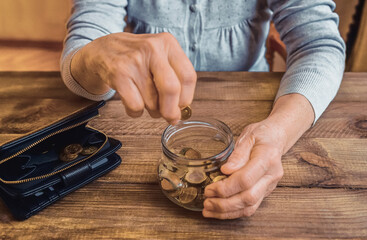 Old wrinkled hand holding jar with coins, empty wallet, wooden background. Elderly woman throws a coin into a jar, counting. Saving money for future, retirement fund, pension, poorness, need concept.