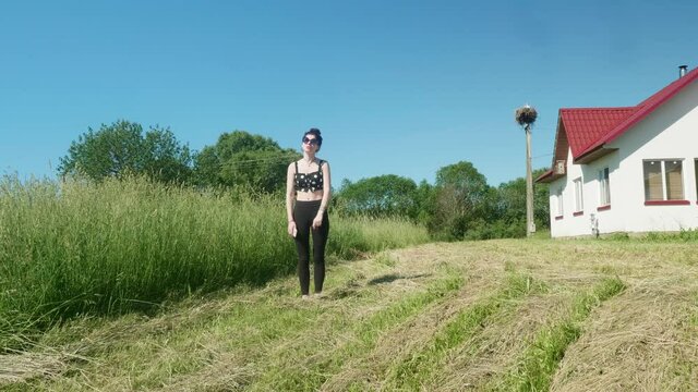 View of young pretty brunnette doing ballet in green fields on sunny summer day.