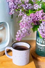 lilac bouquet and coffee mug on the background of the coffee maker