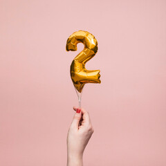 Female hand holding a number 2 birthday anniversary celebration gold balloon