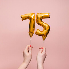 Female hand holding a number 75 birthday anniversary celebration gold balloon