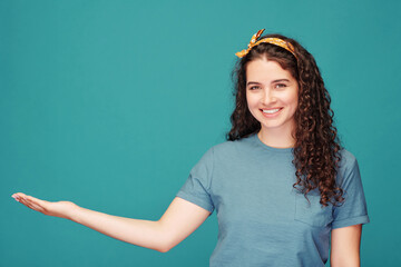 Portrait of smiling pretty woman with curly hair pointing aside while recommending product against...