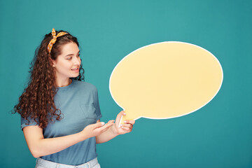 Smiling student girl with curly hair holding speech bubble banner while making presentation against blue background