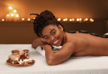 Attractive happy black lady getting hot stones massage