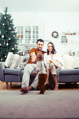 Obraz premium young happy family at home on coach waiting for Christmass with decorated tree, lifestyle people at holiday concept