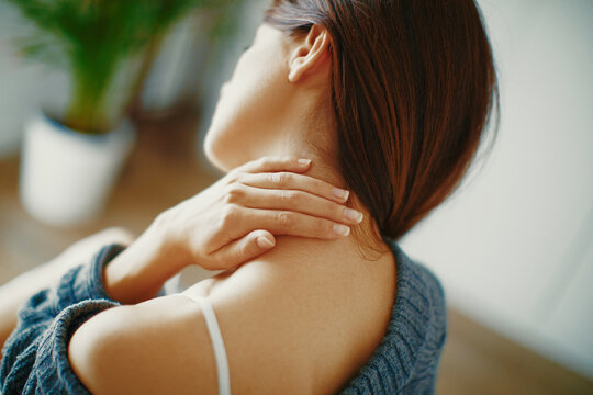 Close up of a brunette woman massaging her neck in a bedroom