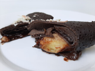 Dadar Gulung Pisang Cokelat, or Rolled Sweet Omelette Filled With Banana and Chocolate Sauce. Traditional snack from Indonesia. Isolated in white background. Top view or flat lay