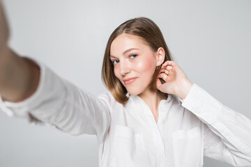 Portrait of smiling attractive woman taking a selfie while isolated over white background