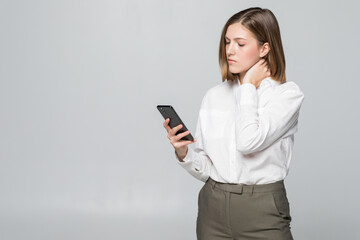 Young businesswoman looking in phone screen holding neck of pain isolated on white background