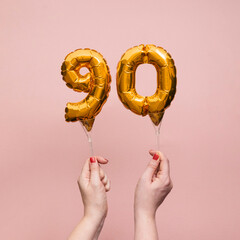 Female hand holding a number 90 birthday anniversary celebration gold balloon