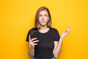 Portrait of smiling business woman using phone holding smartphone and looking back over yellow background.