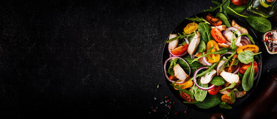 Spring salad with spinach, grilled chicken, cherry tomatoes, arugula, corn salad and red onion. Healthy food concept. Black stone table. Top view. Panoramic banner with place for text