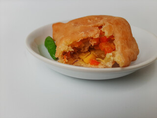 Bitten pastel. Pastel is a popular snack from Indonesia. A pastry filled with chicken meat and mixed vegetable, then deep fried. Served with green chili. On white plate. Isolated in white background.