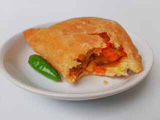 Bitten pastel. Pastel is a popular snack from Indonesia. A pastry filled with chicken meat and mixed vegetable, then deep fried. Served with green chili. On white plate. Isolated in white background.