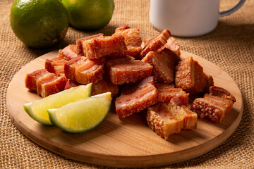 Deep fried crispy pork belly served with two half lemon on the table.