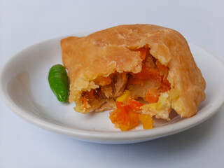 Bitten pastel. Pastel is a popular snack from Indonesia. A pastry filled with chicken meat and mixed vegetable, then deep fried. Served with green chili. On white plate. Isolated in white background.