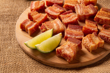 Deep fried crispy pork belly served with two half lemon on the table.