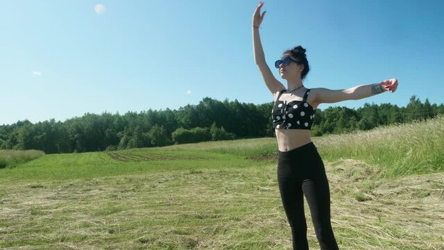 View of young pretty brunnette doing ballet in green fields on sunny summer day.