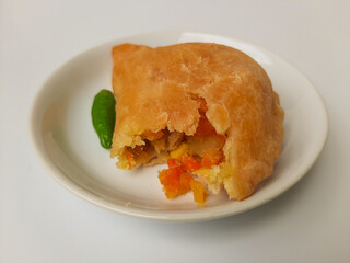 Bitten pastel. Pastel is a popular snack from Indonesia. A pastry filled with chicken meat and mixed vegetable, then deep fried. Served with green chili. On white plate. Isolated in white background.