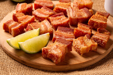 Deep fried crispy pork belly served with two half lemon on the table.