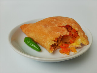 Bitten pastel. Pastel is a popular snack from Indonesia. A pastry filled with chicken meat and mixed vegetable, then deep fried. Served with green chili. On white plate. Isolated in white background.