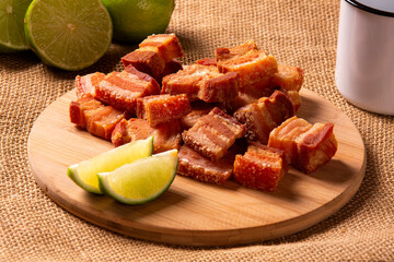 Deep fried crispy pork belly served with two half lemon on the table.