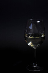 Glass of white wine on a black background. Vertical photo
