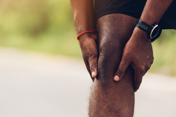 Close up Asian young sport runner black man wear watch stand use hands joint hold knee pain during the run while running at the outdoor street health park, healthy exercise injury from workout concept - obrazy, fototapety, plakaty
