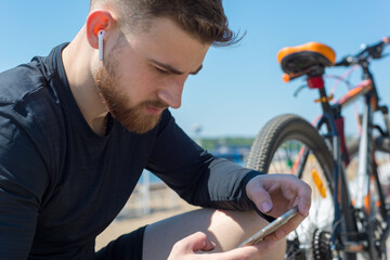 Portrait of a bearded cyclist athlete guy resting after a bike ride using a smartphone in his hand....