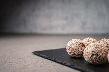 Vegetarian truffles from dates and white sesame on a slate Board near the copy space close-up