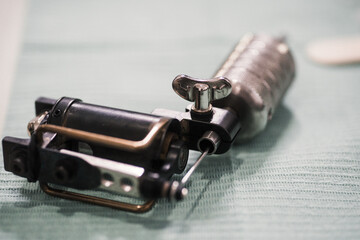 Maquina de tatuar clásica apoyada en una mesa con papel verde preparada para ser utilizada