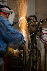 A welder grinding and welding on a metal pipe piece for industrial use
