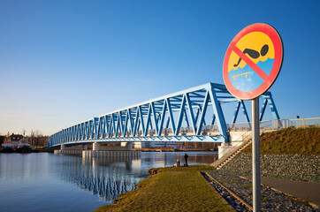 No swimming sign by Odra River in Szczecin sunset, Brdowski Bridge in background, Poland.
