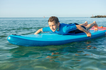 Happy teen child boy having fun and making sport on sup board in Baltic sea