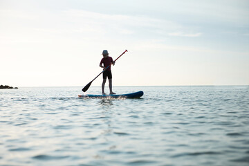 Fototapeta na wymiar Happy teen girl paddling on sup board in Baltic sea