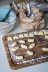Forming gnocchi with fork on wooden board on white background.