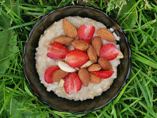 Oatmeal Porridge with Strawberries and muts in bowl on the grass. Healthy Breakfast with Oatmeal...