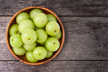 Indian gooseberry fruits ( Amla, phyllanthus emblica ) in wooden bowl isolated on old rustic wood table background. Top view. Flat lay.