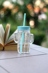 Cactus shaped bottle with cold water and open book in a garden. Selective focus.