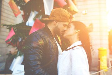 Fototapeta na wymiar Stylish young couple of hipsters kissing near Christmas tree during their walk in the city. Romantic honeymoon in Barcelona for the newlyweds. Love and tenderness of these young people are limitless