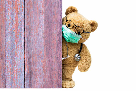 Brown teddy bear doctor with protective medical mask and stethoscope behind the old wooden door or window. Quarantine coronavirus pandemic prevention,  covid-19 concept.